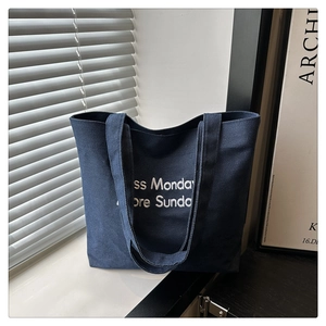 Macro detail of navy blue canvas tote bag featuring white Less Monday More Sunday embroidery