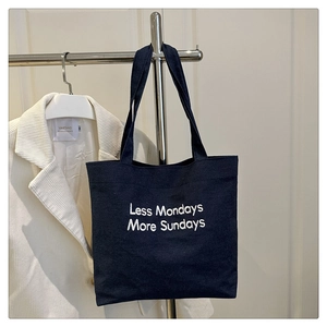 Detail of dark blue canvas tote bag with white embroidery Less Mondays More Sundays