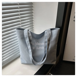 Detailed view of light blue canvas tote bag featuring premium white letter embroidery