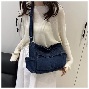 Detail of dark blue denim crossbody bag with flap pockets and wide adjustable strap