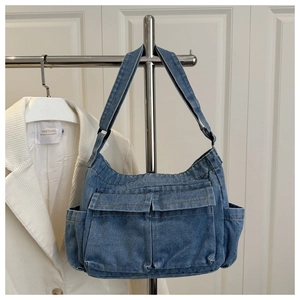 Detail view of washed blue denim shoulder bag with multiple functional utility pockets