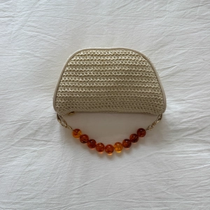 Close-up of beige woven straw handbag featuring amber resin bead handle and gold chain details