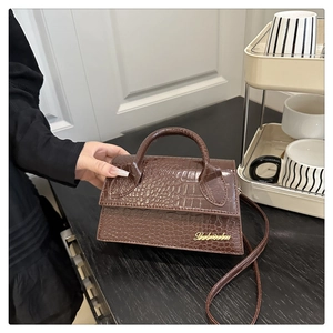 Detail of dark brown croc-embossed leather crossbody bag with golden metal logo accent