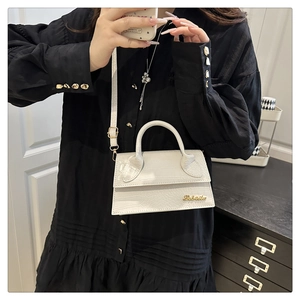 Close-up of white crocodile pattern bag with gold logo on black pleated shirt background