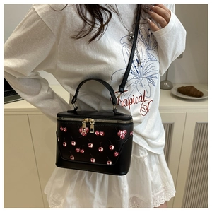 Detail of a black box handbag with cherry prints and gold zippers worn by a model