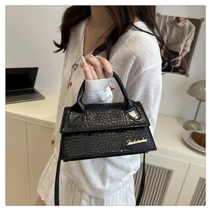 Detail of black crocodile pattern leather handbag with gold logo and white outfit