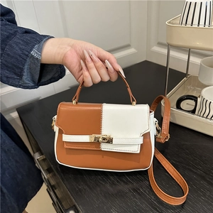 Fashionable contrast color saddle bag with top handle and brown strap on wooden table
