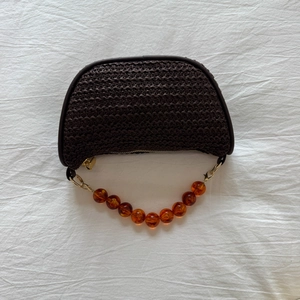 Detail of hand-woven coffee brown straw bag with amber resin bead chain handle
