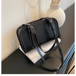 Detailed view of black leather crossbody bag with white contrast stitching and gold text
