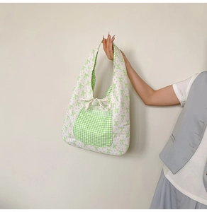 Detail of floral tote bag with green plaid pocket and bow on white fabric texture