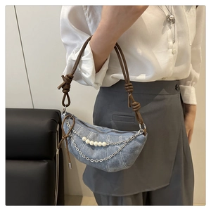 Dettaglio borsa a mezzaluna in denim celeste con catene metalliche, perle e pelle marrone