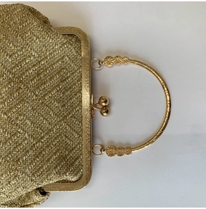 Detailed view of golden woven evening clutch with ornate floral engraved kiss-lock frame