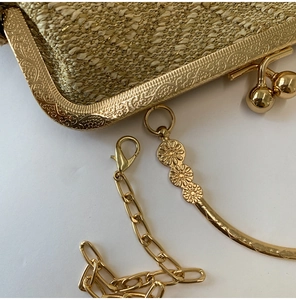 Detail of gold woven evening bag with embossed metal frame and daisy chain charm