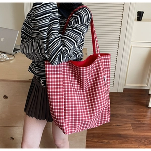 Side view of woman carrying a large red checkered canvas tote bag in a cozy home setting