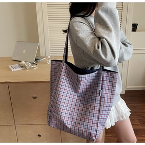Close-up of a large plaid fabric tote bag in a casual office setting with a laptop