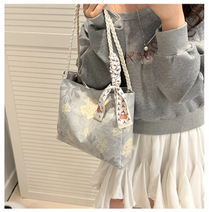 Détail d'un sac en toile bleu clair à motif floral avec anses tissées et foulard