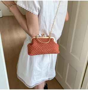 Detail of orange woven shell bag with golden spherical clasp and metal chain strap