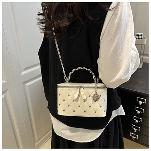 Détail d'un mini sac matelassé blanc avec chaîne argentée et breloque fleur sur le modèle
