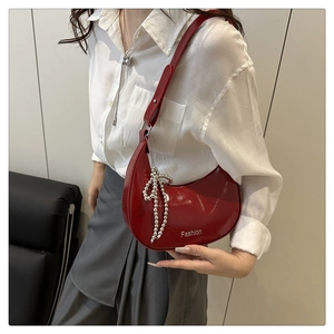 Red patent leather crescent bag detail with silver Fashion text and beaded bow charm