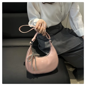 Detail of pink glossy leather hobo bag featuring a silver bead bow charm and fashion logo