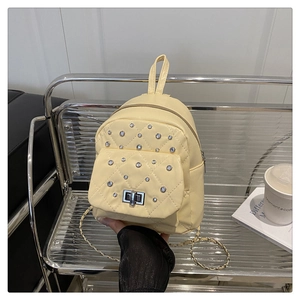 Détail d'un petit sac à dos jaune clair matelassé avec strass et bandoulière chaîne