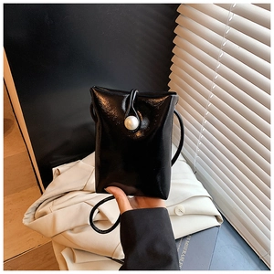 Detail of a mini black glossy crossbody bag featuring a large pearl clasp and slim strap