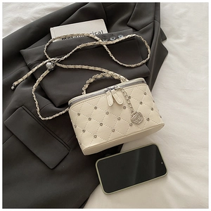 Détail du sac beige matelassé avec pendentif camélia et bandoulière en chaîne