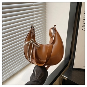 Close-up of a brown crescent shoulder bag with shiny faux leather and beaded bow charm