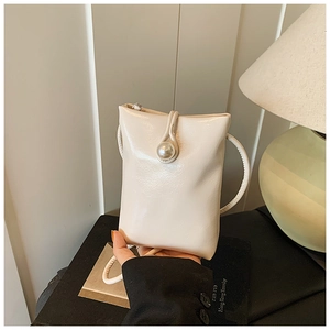 Detail of a mini cream-colored vertical phone bag featuring a large pearl clasp closure