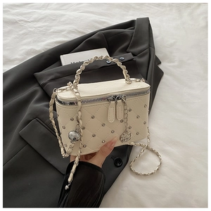 Détail du sac boîte matelassé blanc cassé avec rivets et breloque rose élégante