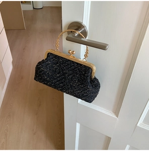 Detailed macro of a black woven evening clutch featuring gold frame and floral handle