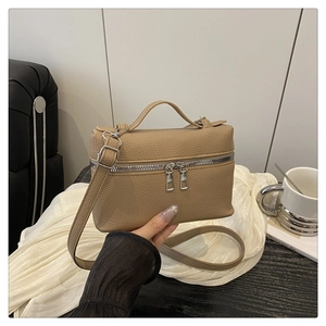 Detail of khaki pebbled leather bag featuring dual silver zippers and top handle
