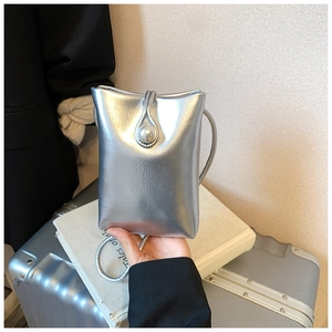Silver metallic crossbody phone bag with pearl closure held against a travel suitcase