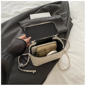 Détail d'un sac caméra blanc matelassé avec clous argentés et bandoulière en chaîne