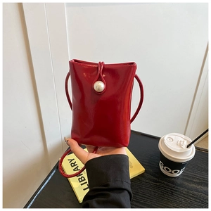 Close-up of stylish red mini crossbody bag with pearl buckle in a cafe setting