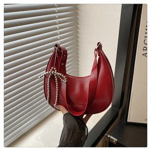 Detail of red crescent shoulder bag with glossy patent leather and silver bead bow charm