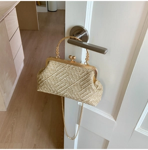 Detail of beige woven shell clutch bag with gold metallic clasp and chain strap