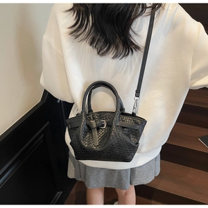 Détail du sac seau noir tressé avec poignées circulaires porté par un mannequin