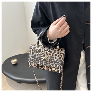 Close-up of leopard print handbag with golden bow metal buckle on a black coat outfit