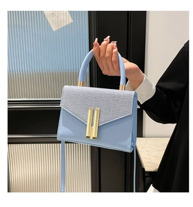 Detail of light blue crossbody bag with gold hardware and textured leather flap