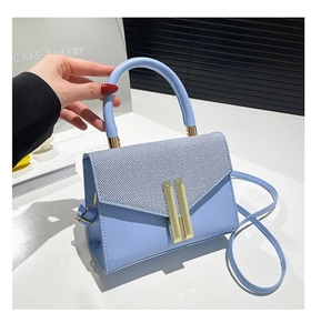 Detail of light blue crossbody bag with woven texture flap and golden hardware