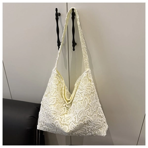Détail du sac cabas en dentelle blanche avec motifs floraux suspendu à une armoire