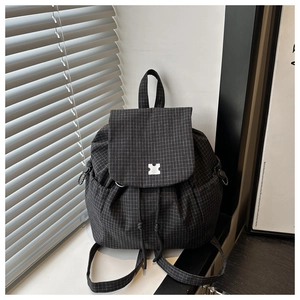 Detail of grid pattern backpack featuring drawstring closure and silver buckle under natural light
