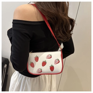 Detail of red strawberry print on white crossbody bag shown on model for sizing
