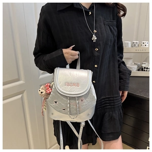 Detail of silver metallic backpack with IBCMB embroidery and plush monkey charm accessory