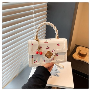 Détail du sac à main blanc à imprimé cerise avec fermoir fleur doré et breloque cerise