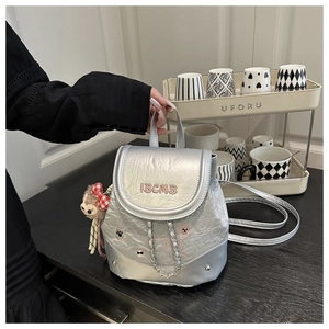 Detail of silver metallic backpack with pink embroidery, metal chains and monkey charm