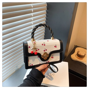 Détail du sac cerise avec poignée tressée et fermoir trèfle doré élégant