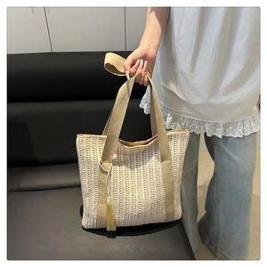 Detail of woven straw tote bag with khaki canvas straps and yellow tassel accent