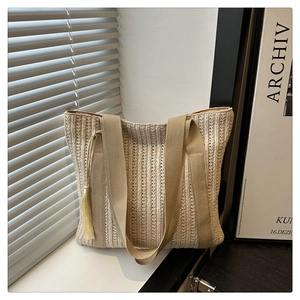 Detail of woven straw tote bag with canvas straps and yellow tassels in soft sunlight